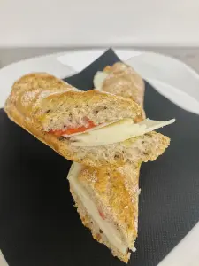 Bocadillo cortado por la mitad, mostrando su relleno de queso y tomate, colocado sobre una servilleta negra en un plato blanco.